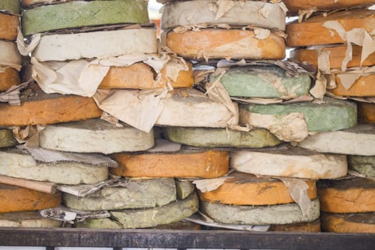 Different types of cheese wheels are stacked high in a vibrant market.