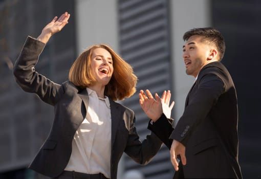 Two business partners celebrating success outdoors, raising their hands in excitement and smiling