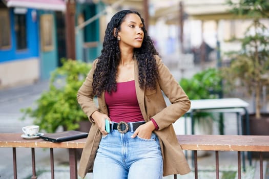 A stylish young woman with curly hair stands outdoors, confidently posing in a chic outfit that highlights her unique fashion style, radiating elegance and selfassurance in a natural setting