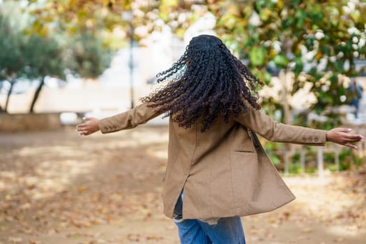 In a beautiful, serene outdoor setting, a woman with lovely, curly hair twirls joyfully, radiating happiness and freedom, while surrounded by vibrant autumn leaves and lush greenery all around her