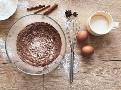 Making spicy chocolate dough. Ingredients for baking the sponge cake are laid out on a wooden table. View from above.