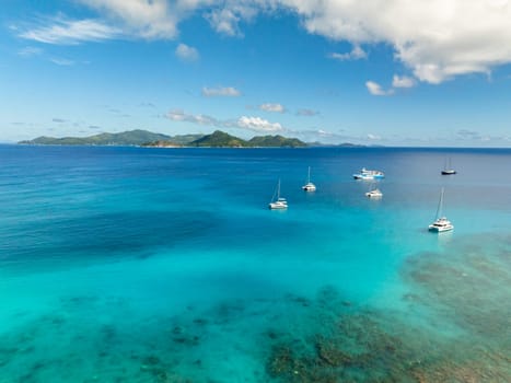 Boats floating on calm turquoise waters, distant green islands and a peaceful horizon. La Digue, Seychelles.