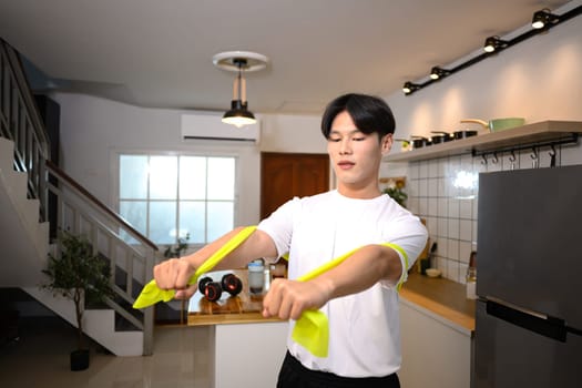 Active man in casual fitness wear working out with a resistance band in his home.