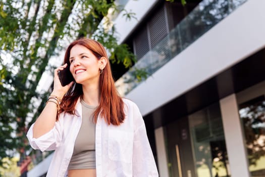 young woman smiling happy while walking down the street in a good mood talking on cell phone, concept of technology of communication and urban lifestyle, copyspace for text