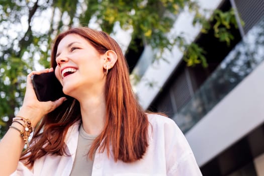 young woman laughing happy while walking down the street in a good mood talking on cell phone, concept of technology of communication and urban lifestyle, copyspace for text