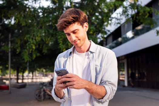 smiling man using his cell phone while walking down the street, he is wearing a white shirt and is focused on his phone, concept of technology of communication and urban lifestyle, copyspace for text