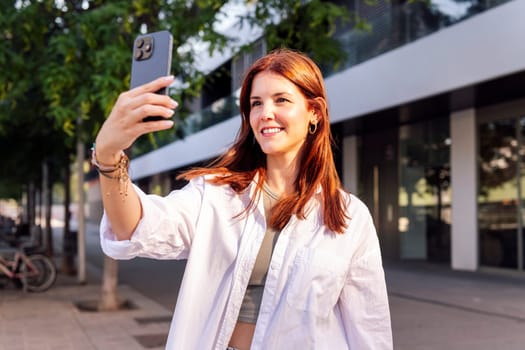 smiling young woman taking a selfie with cell phone, she is happy and enjoying the moment, concept of technology of communication and urban lifestyle