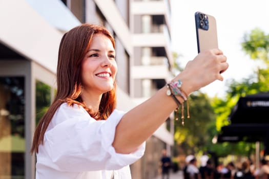 smiling young woman taking a selfie with cell phone, she is happy and enjoying the moment, concept of technology of communication and urban lifestyle