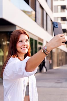 smiling young woman taking a selfie with cell phone, she is happy and enjoying the moment, concept of technology of communication and urban lifestyle