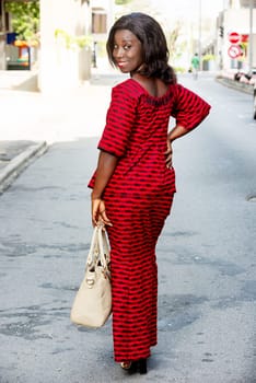 African woman standing in the street and looking back at the camera smiling. woman concept in red loincloth or african fashion