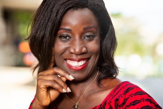outdoor portrait of a beautiful young African woman in a red loincloth outfit and with long hair, stands the mint with hand in the street looking at the camera,