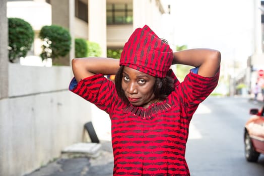 fashionable stylish african woman wearing a red loincloth straps a scarf on her head while smiling in the street in daylight