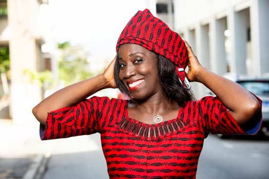 mature african woman standing outdoors adjusting her scarf and looking at the camera smiling.
