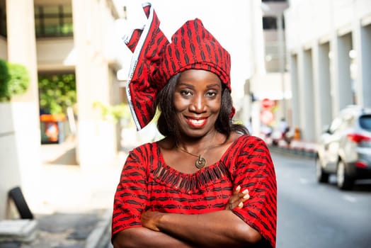 mature african woman standing outdoors head tied with a piece of loincloth watching the camera smiling.