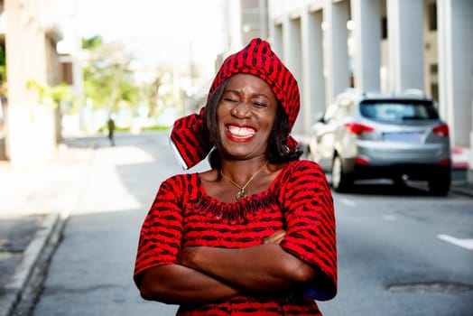 mature african woman standing outdoors head tied with a piece of loincloth watching the camera laughing.