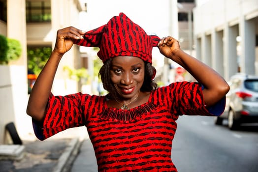 mature african woman standing outdoors adjusting her scarf and looking at camera smiling.