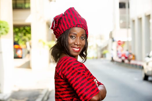 mature african woman standing outdoors looking at the profile camera smiling with arms crossed.