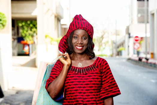 mature woman in loincloth standing outdoors holding shopping bags while smiling.