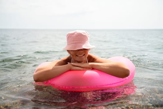 A woman is laying on a pink inflatable raft in the ocean. The scene is peaceful and relaxing, with the woman enjoying the water and the sun