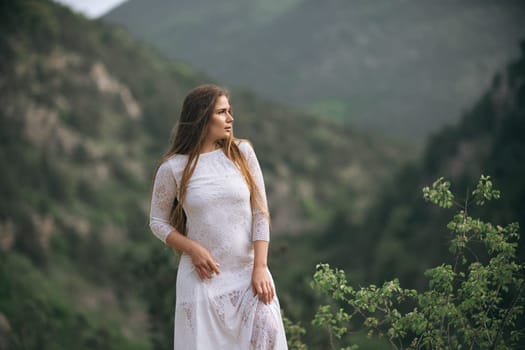 A woman in a white dress is standing on a mountain. The image has a serene and peaceful mood, as the woman is alone and surrounded by nature
