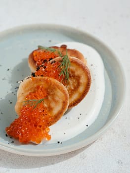Pancakes served with red caviar. Delicious pancakes on sour cream on blue plate decorated natural red caviar of fish. Close up Vertical.