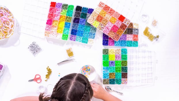 Flat lay. Delicate fingers of a young girl navigate through a treasure trove of bright, multicolored beads, each compartment revealing a new hue to choose from.