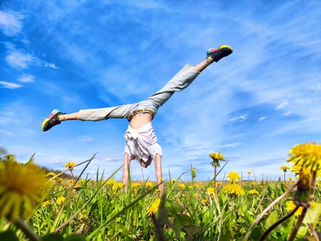 A person executes a handstand among vibrant dandelions, enjoying the sunny weather and open sky.