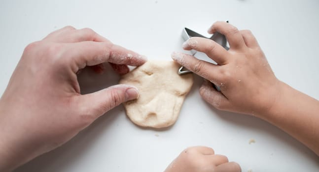 Child and adult hands crafting dough with cookie cutter on white surface.