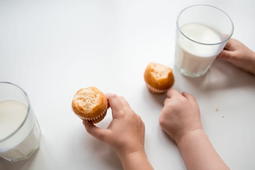 Child hands holding muffins and milk on white background.