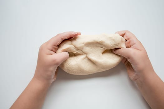Child hands kneading dough on white surface.