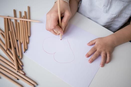 Child drawing heart with pencils on paper.