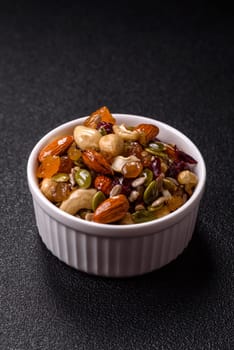 Honeyed cashew nuts, walnuts, hazelnuts, pine nuts and dried fruits in ceramic bowl on dark concrete background
