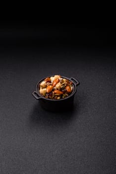 Honeyed cashew nuts, walnuts, hazelnuts, pine nuts and dried fruits in ceramic bowl on dark concrete background