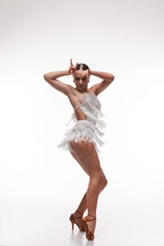 Elegant female dancer in white fringe outfit performing Latin dance pose on white background.