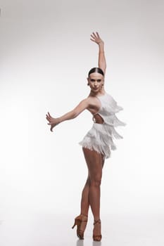 Elegant female dancer in white fringe outfit performing Latin dance pose on white background.