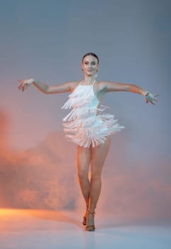 Elegant female Latin dancer in a white fringed dress performing a dynamic move with grace and confidence in artistic lighting.