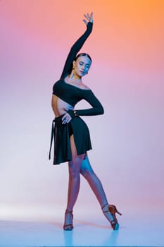 Stylish female dancer in black outfit posing in Latin dance move on vibrant gradient studio background.