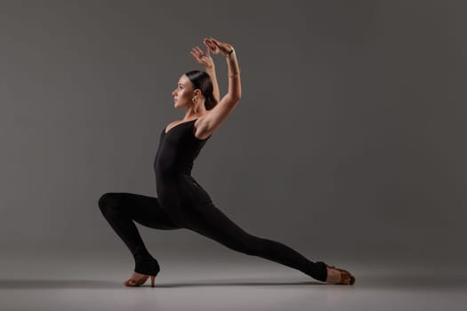 Female dancer in black bodysuit performing contemporary Latin dance pose on gray studio,