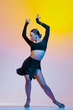 Stylish female dancer in black outfit posing in Latin dance move on vibrant gradient studio background.