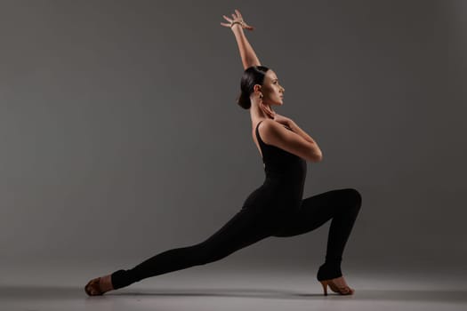Female dancer in black bodysuit performing contemporary Latin dance pose on gray studio,