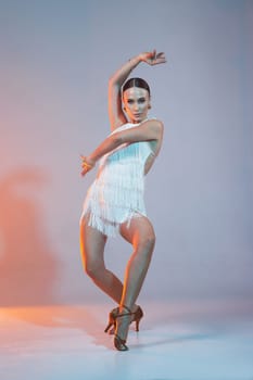 Elegant female Latin dancer in a white fringed dress performing a dynamic move with grace and confidence in artistic lighting.