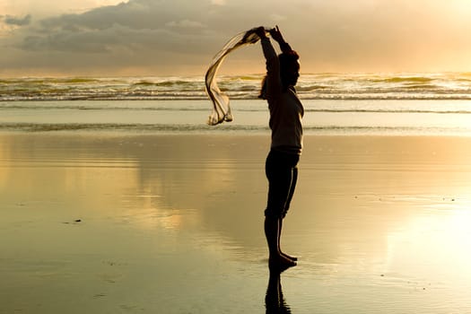 A woman lets a scarf blow in the wind at sunset on the beach in Newport, Oregon.