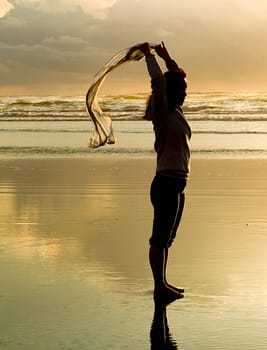 A woman lets a scarf blow in the wind at sunset on the beach in Newport, Oregon.