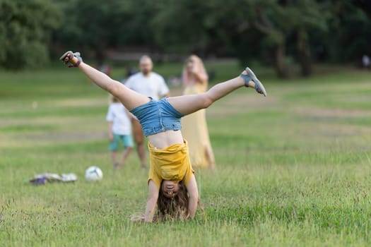 Girl practicing cartwheel in park with family watching, enjoying summer activity and healthy lifestyle