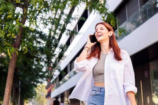 young woman laughing happy while walking down the street in a good mood talking on cell phone, concept of technology of communication and urban lifestyle, copyspace for text