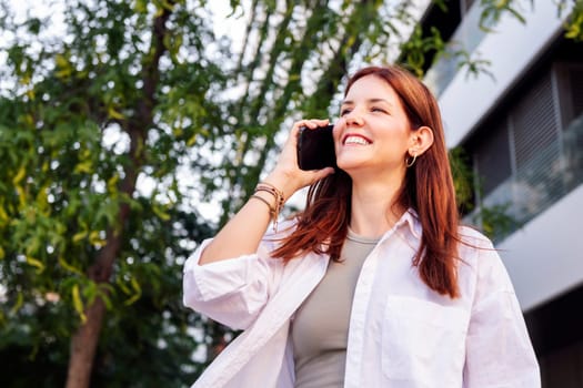 young woman smiling happy while walking down the street in a good mood talking on mobile phone, concept of technology of communication and urban lifestyle, copyspace for text