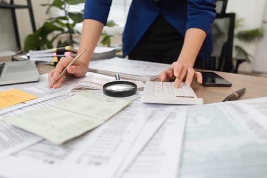 A diligent accountant calculates taxes using a calculator and magnifying glass, surrounded by financial papers.