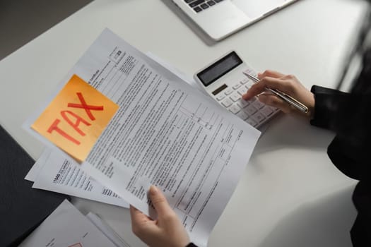 A focused businesswoman reviews tax documents while using a calculator, highlighting the importance of accurate tax filing.