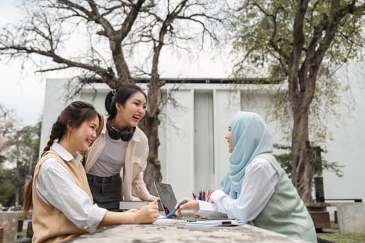 A diverse group of university students laughing and collaborating outdoors while studying, surrounded by trees and academic materials.