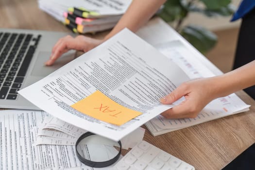 A professional woman reviews tax documents while working on her laptop, emphasizing her role in finance and accounting.